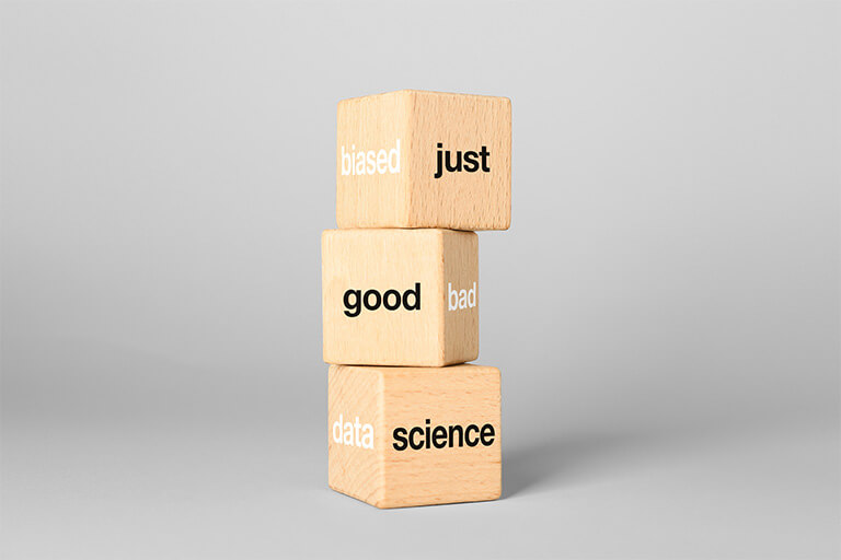 Photograph of a tower of three wooden cubes with black and white writing on visible sides. In black: just, good, science In white: biased, bad, data